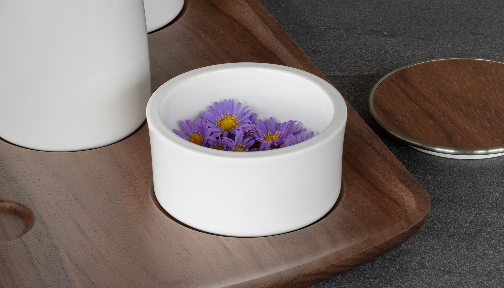 Porcelain container filled with aster flowers on walnut tray